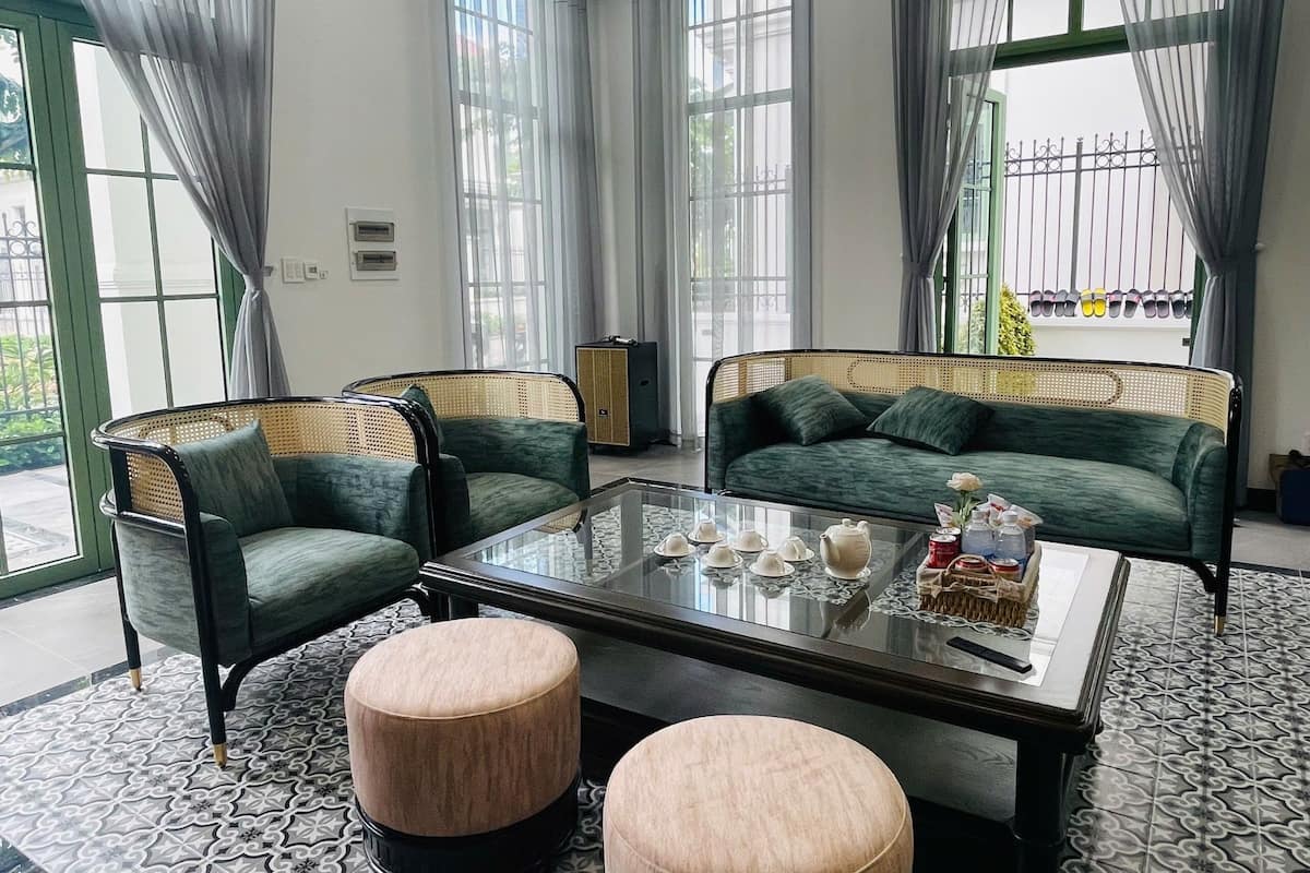 A modern living room with two green sofas, a glass coffee table, and two round ottomans.