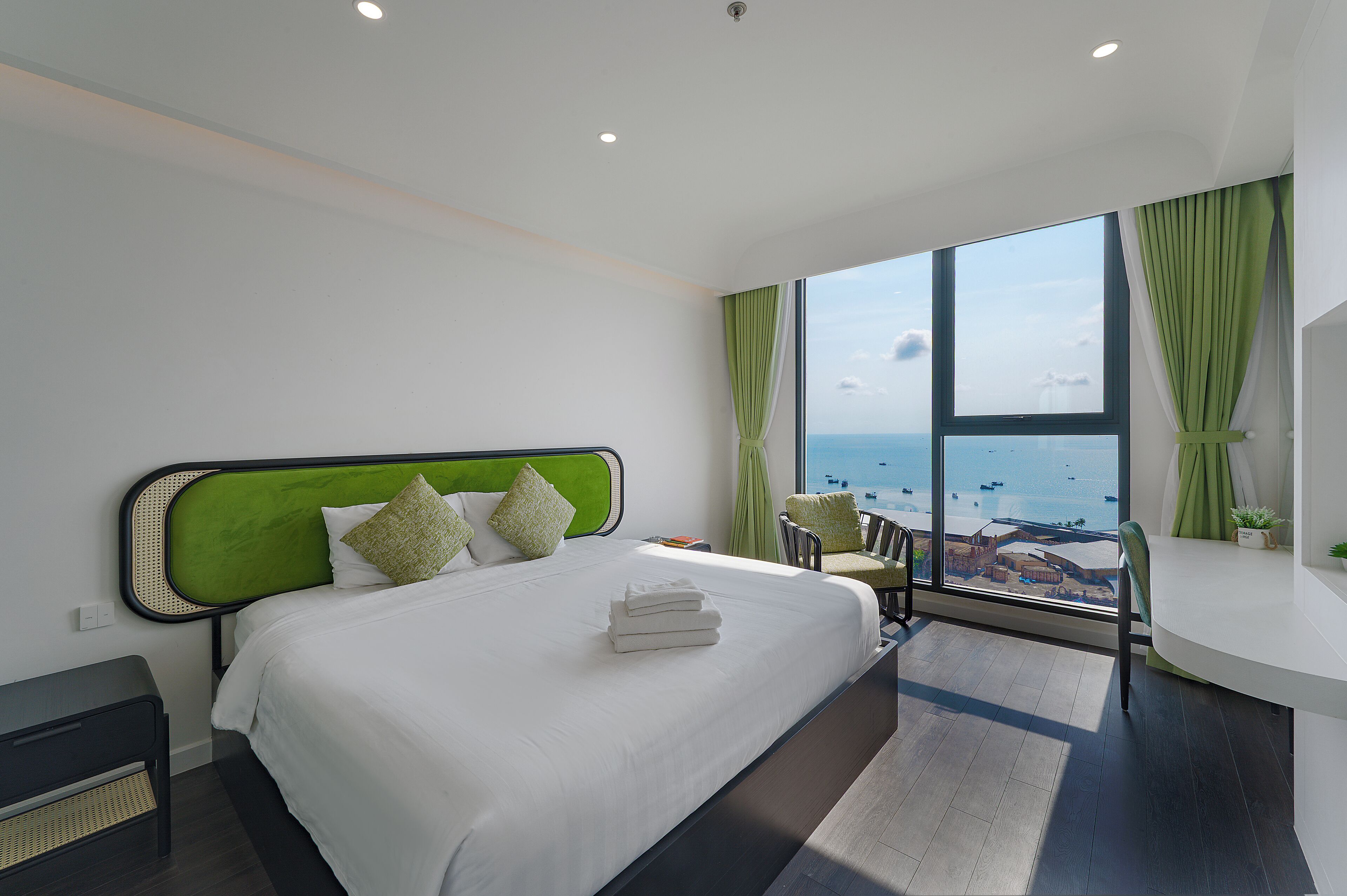 A modern hotel room with a large bed, a view of the sea, and a seating area with a view.
