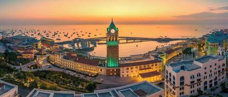 A coastal cityscape with a prominent clock tower, a marina with numerous boats, and a well-lit waterfront promenade.