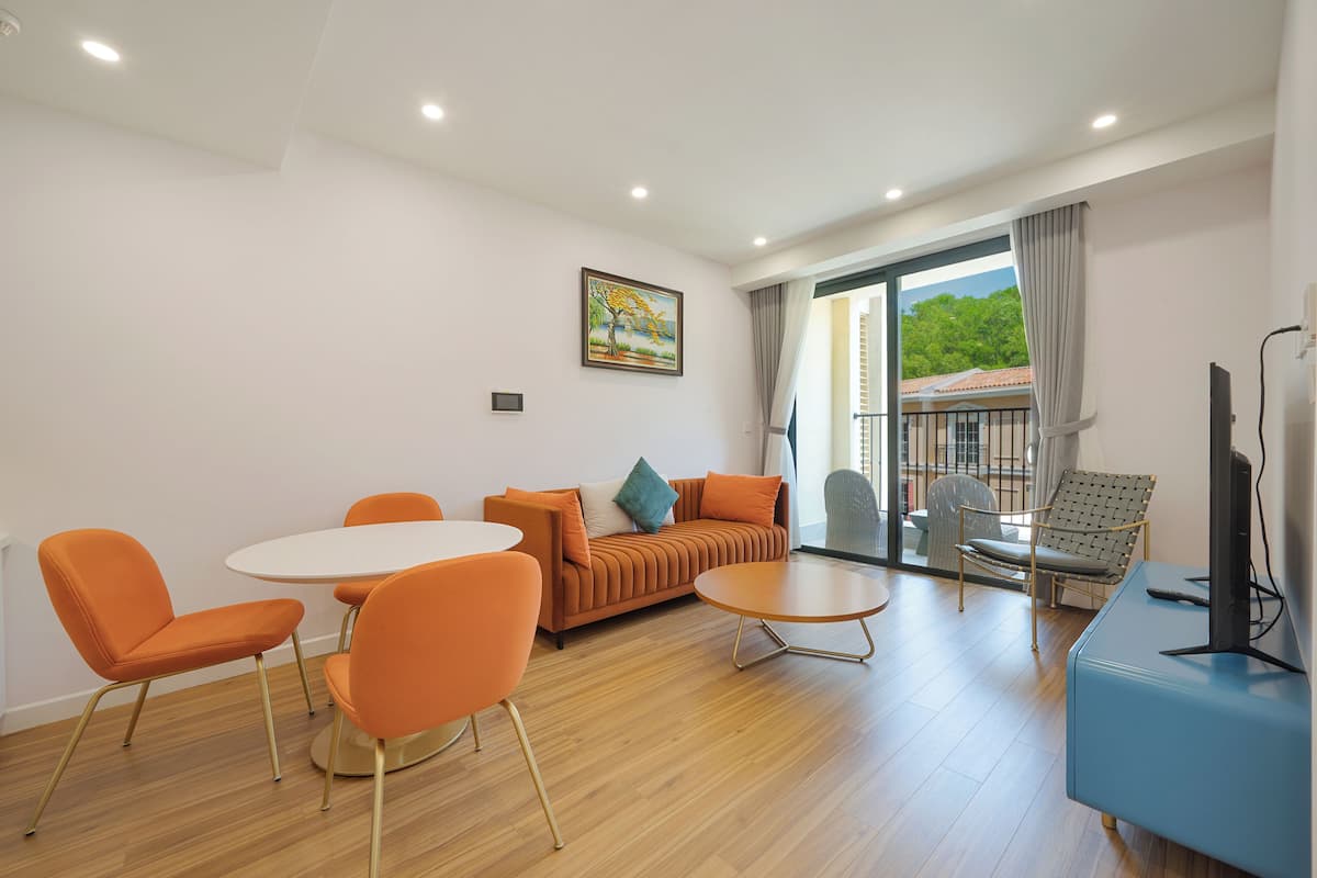 A modern living room with a sofa, two orange chairs, a round table, and a television.