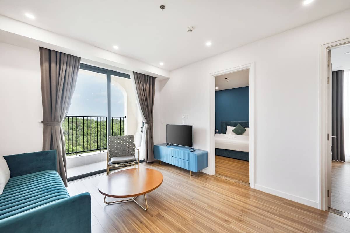 A modern hotel room with a balcony, a TV, a bed, and a seating area.