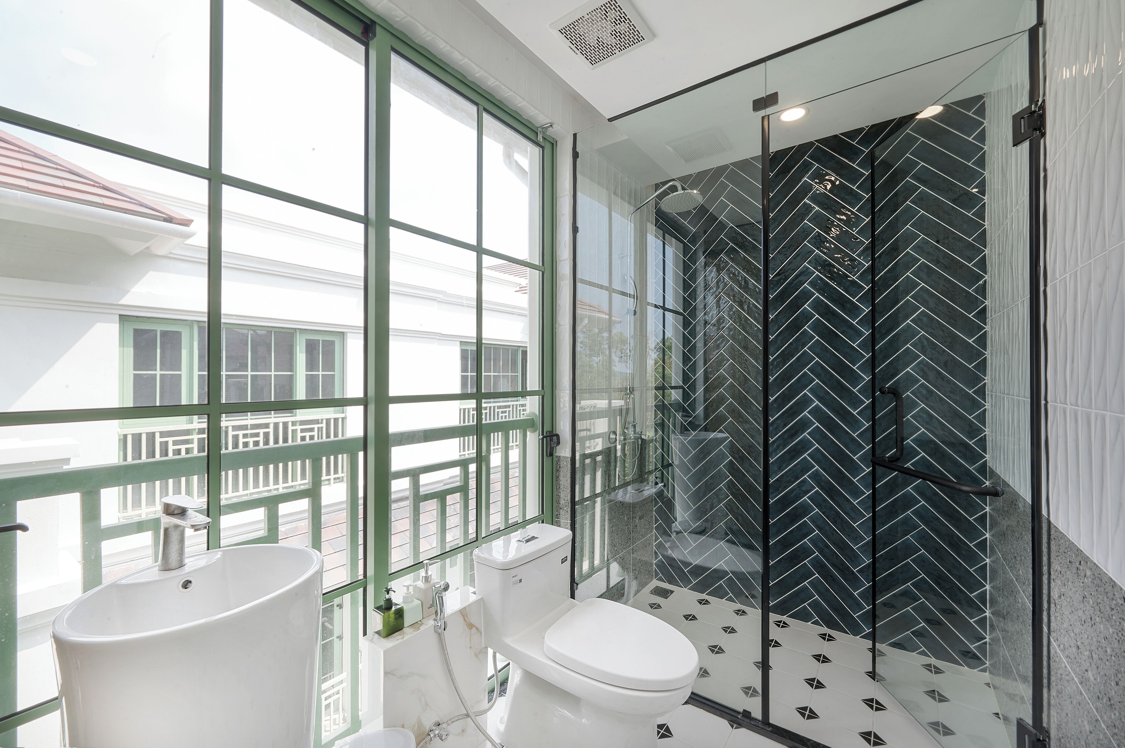 A modern bathroom with a large window, a glass-enclosed shower, and a white sink.