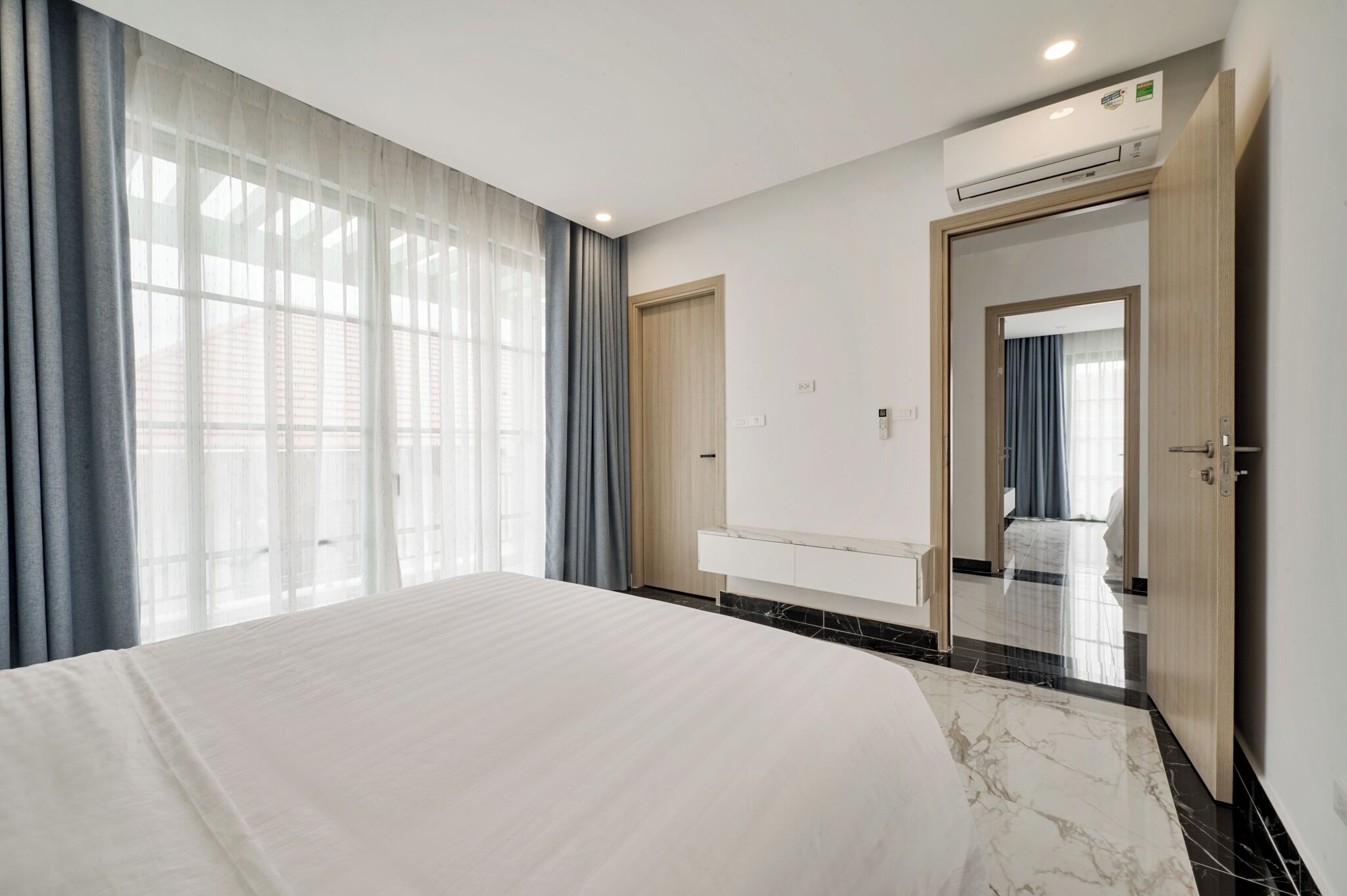 A modern hotel room with a large bed, a built-in desk, and a bathroom visible through an open door.
