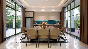 Un comedor moderno con una mesa grande y sillas, una cocina al fondo y amplios ventanales con cortinas.