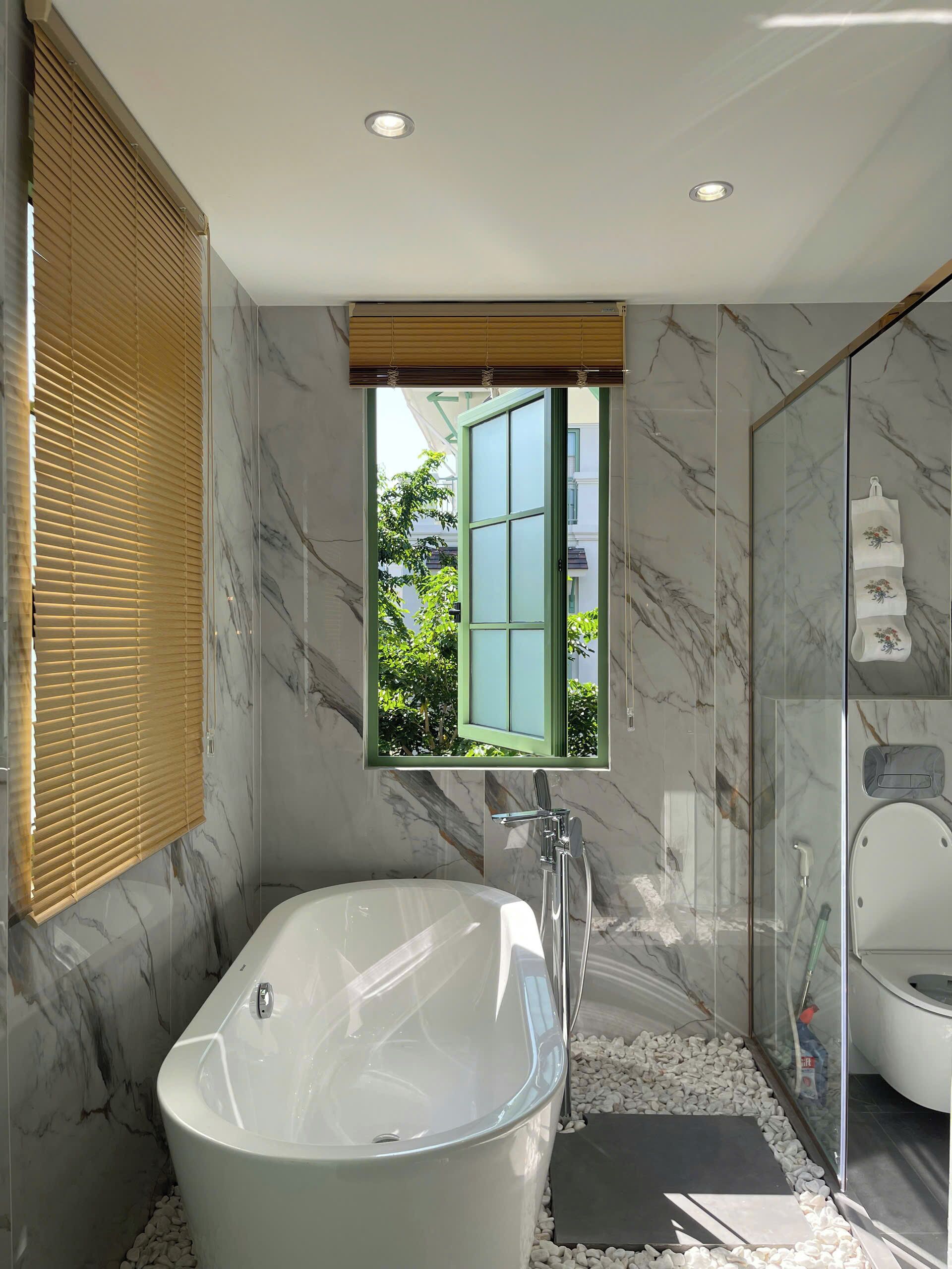A modern bathroom with a freestanding bathtub, a glass-enclosed shower, and a window with a view of greenery.