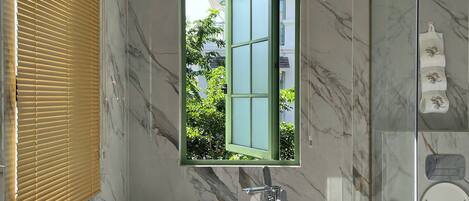 A modern bathroom with a freestanding bathtub, a glass-enclosed shower, and a window with a view of greenery.