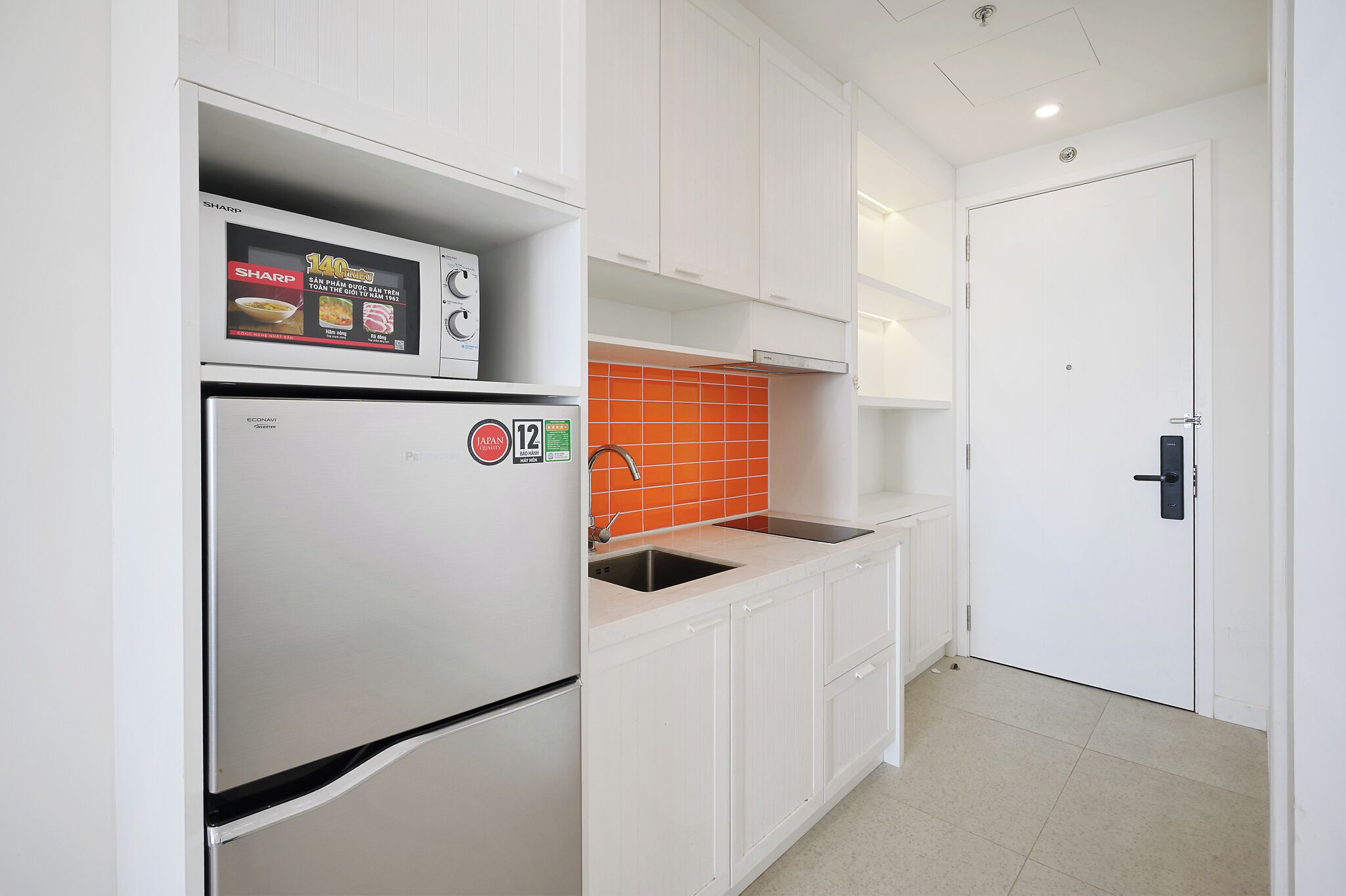Una cocina con armarios blancos, un refrigerador de acero inoxidable, un salpicadero naranja y una puerta blanca.