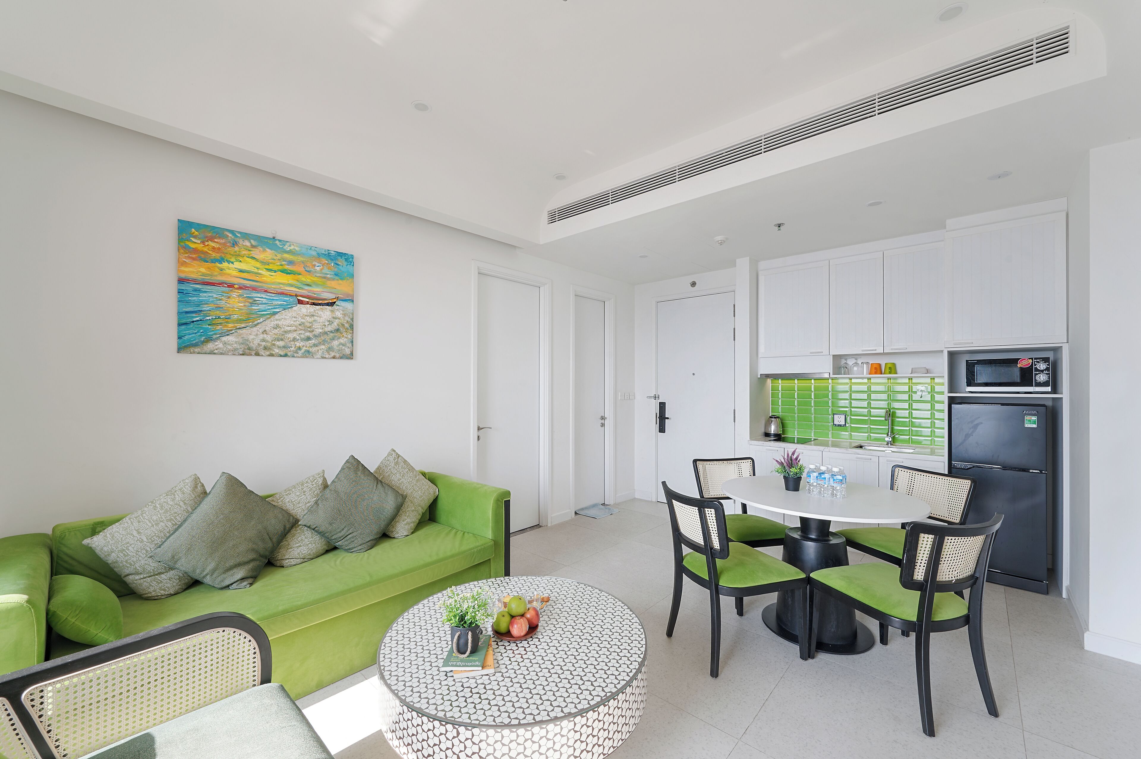 A modern living room with a green sofa, a round coffee table with fruits, and a painting on the wall.