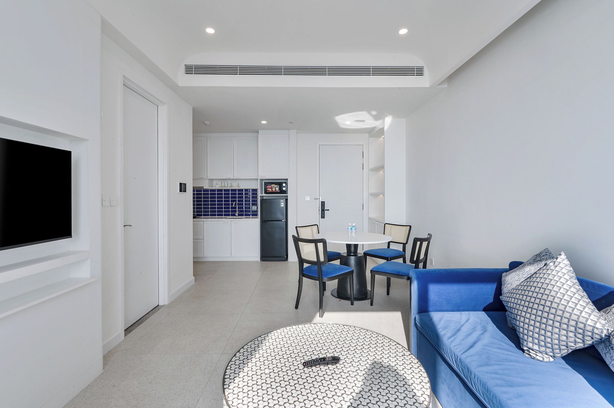 A modern living room with a blue sofa, a round coffee table, and a TV mounted on the wall.