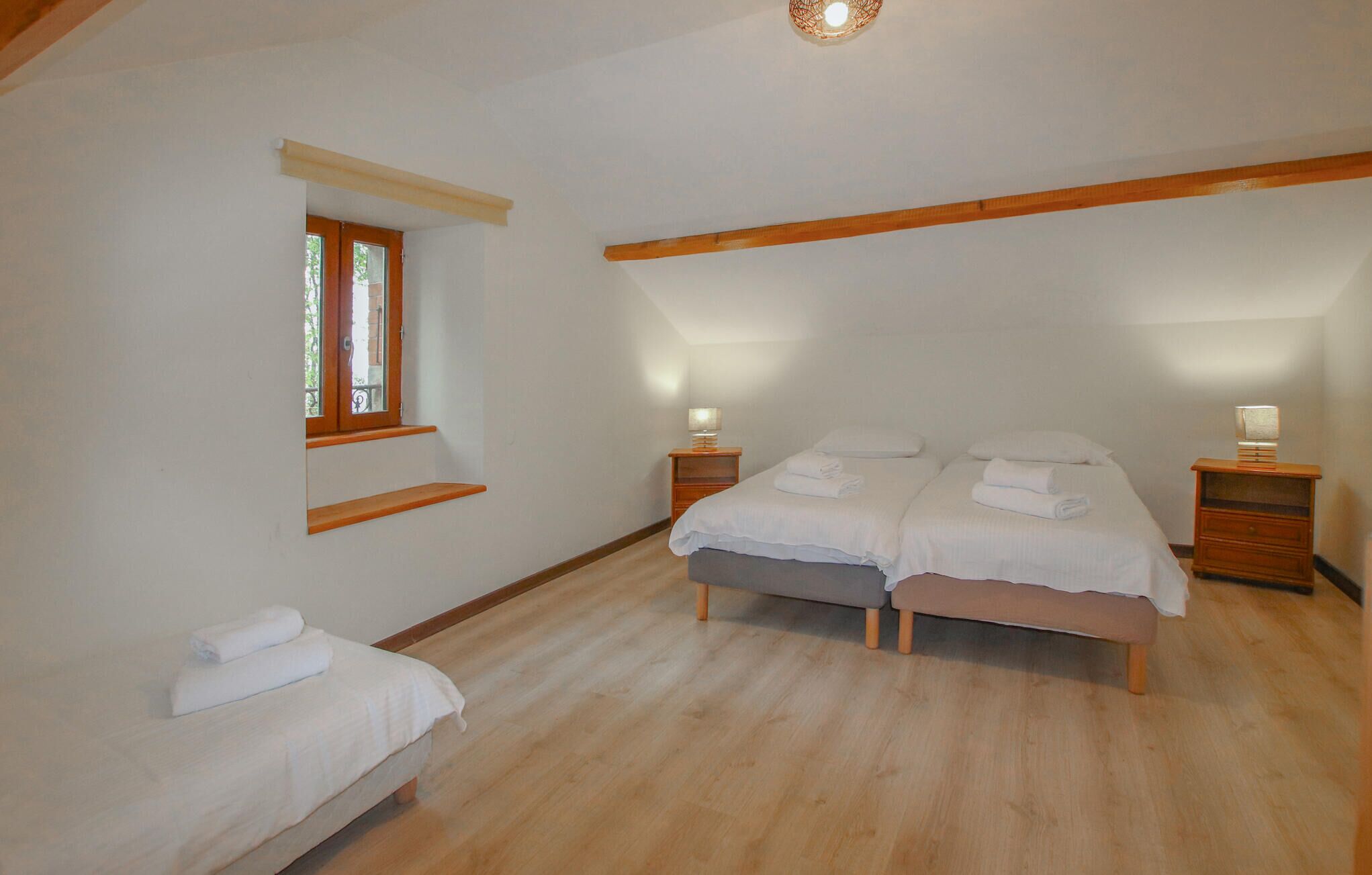 A bedroom with two beds, wooden beams, a window, and bedside lamps.
