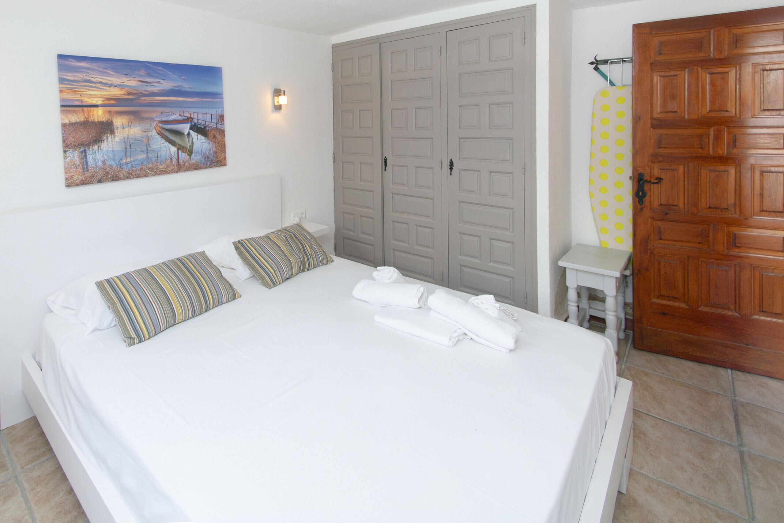 A bedroom with a bed, pillows, a painting, a wardrobe, and a bathroom with a towel rack.