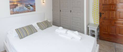 A bedroom with a bed, pillows, a painting, a wardrobe, and a bathroom with a towel rack.