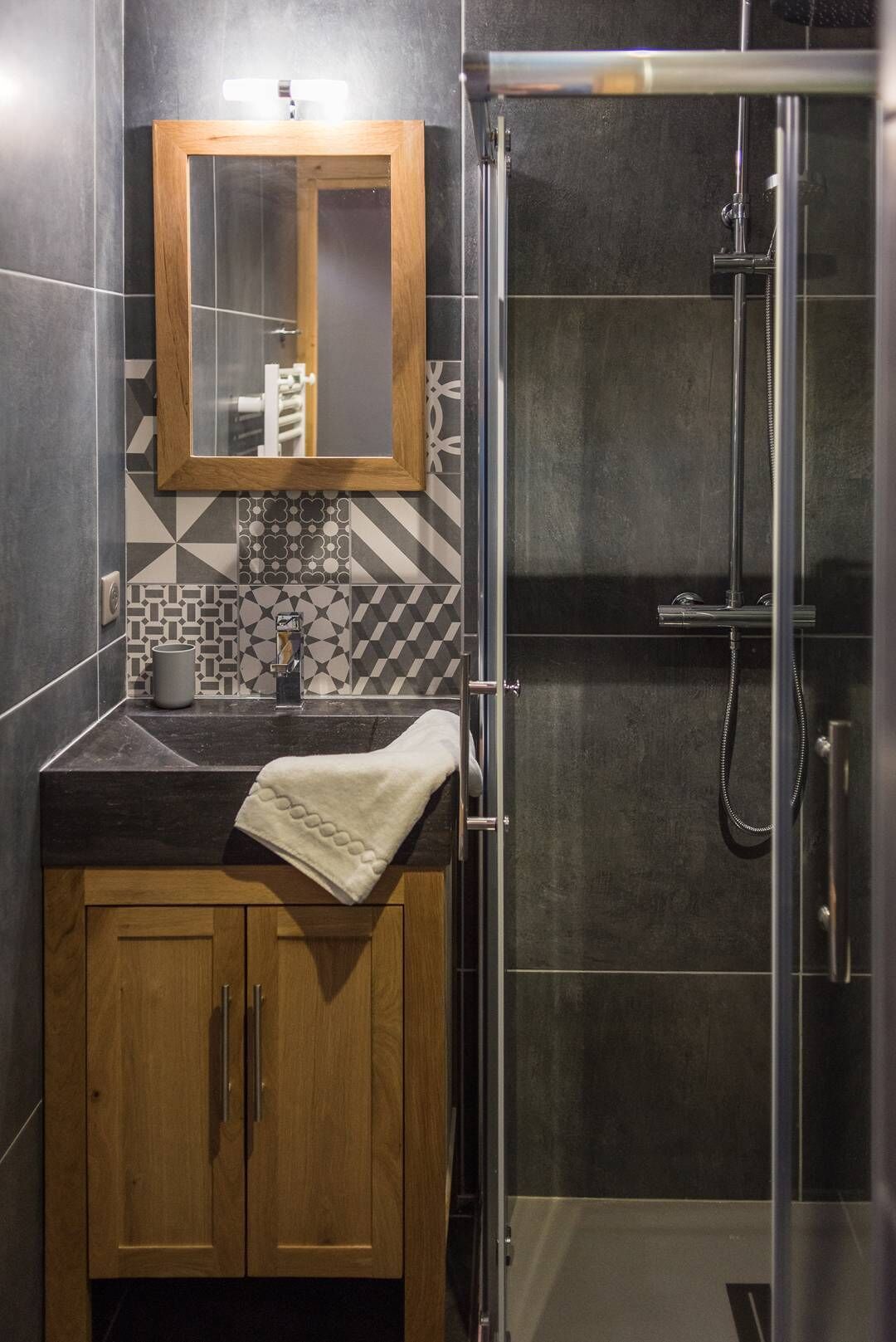 A modern bathroom with a wooden vanity, a mirror, a sink, and a shower enclosure.
