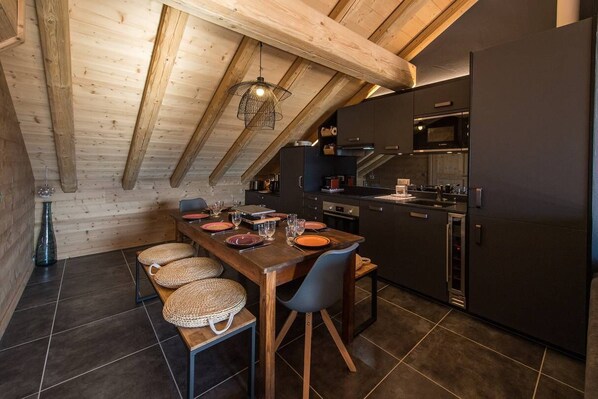 Una cocina moderna con armarios oscuros, una mesa de comedor de madera y un techo alto con vigas a la vista.