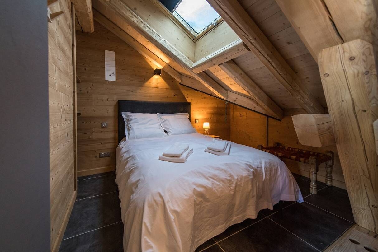 A cozy, wooden bedroom with a skylight, a neatly made bed, and a small bedside table.