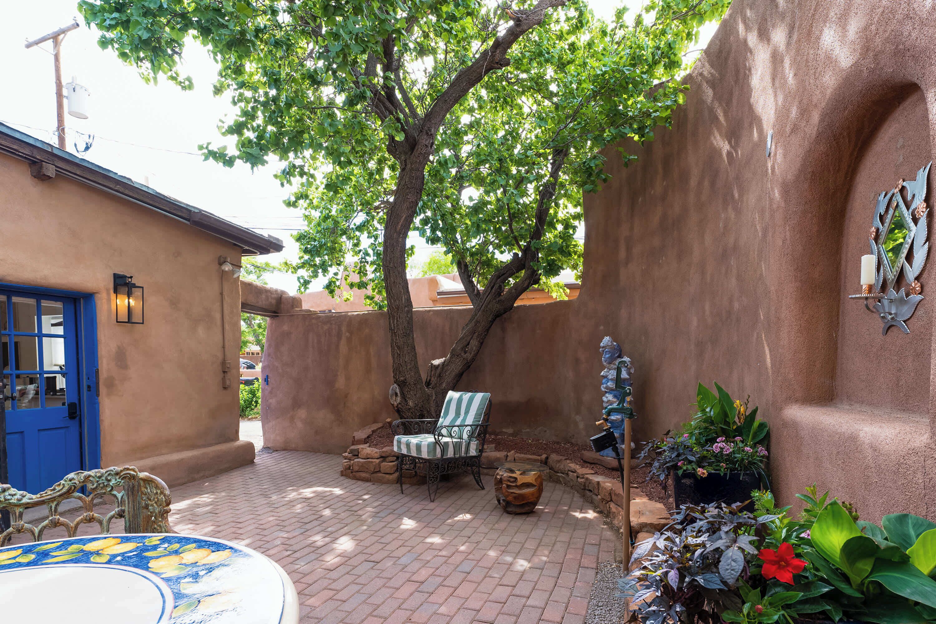 A courtyard with a blue door, a striped chair, a decorative wall, and a potted plant.