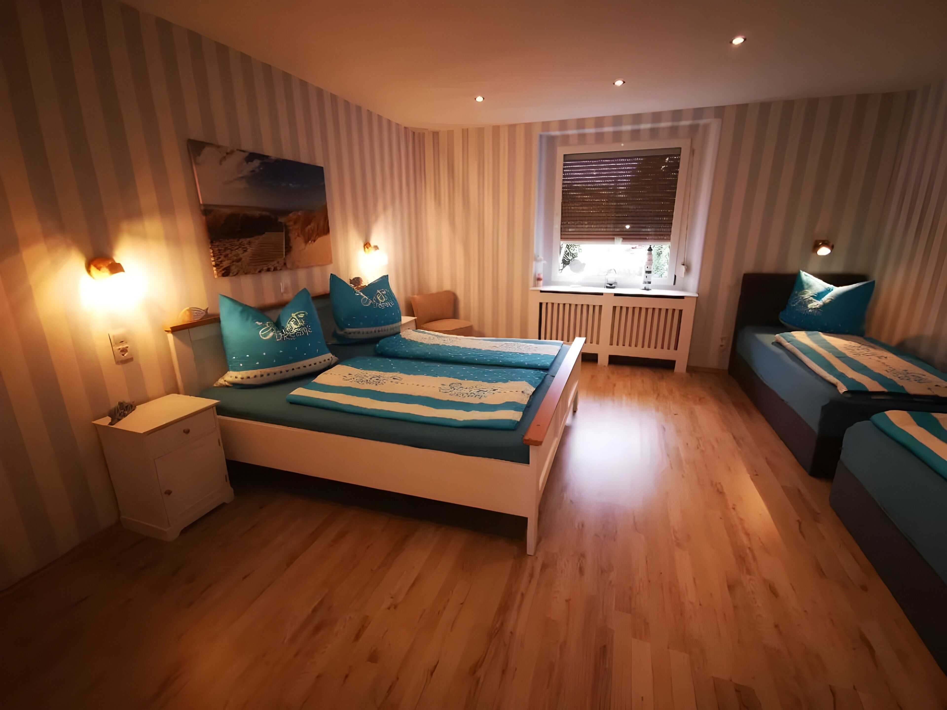 A bedroom with a bed, a bedside table, a chair, a window with blinds, and a radiator.