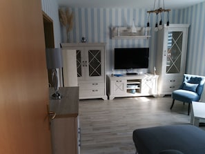 Huoneessa on televisio, kaappi, tuoli ja puulattia.