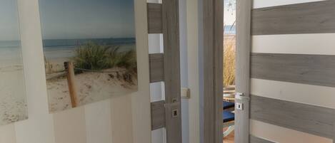 Pintura de una escena de playa en una pared, una puerta de madera y un vistazo a una habitación con una cama.