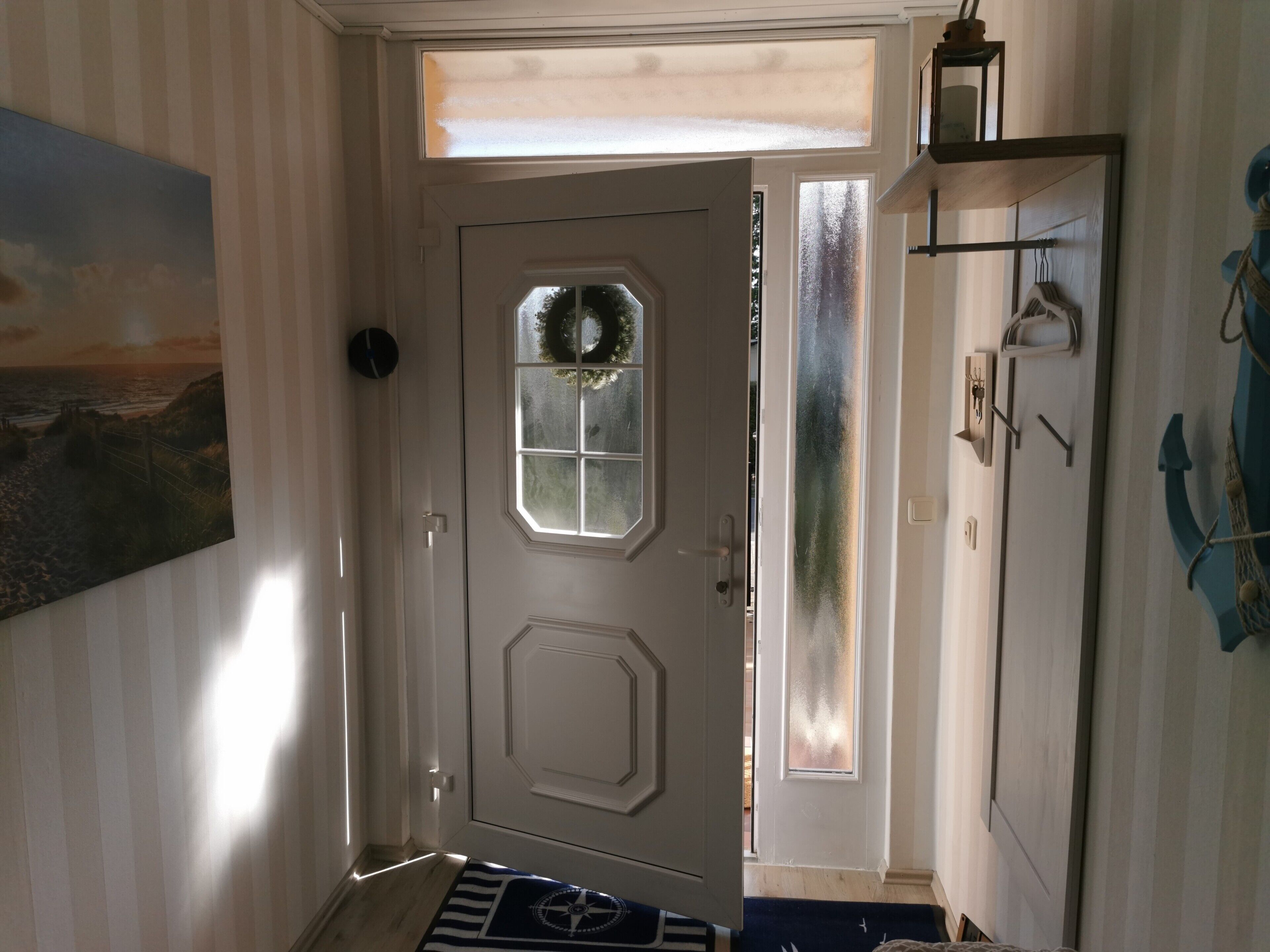 A hallway with a door, a painting, a rug, and a shelf with items.