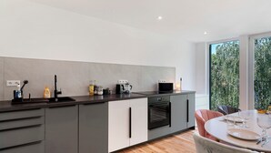 Una cocina moderna con horno empotrado, lavamanos y comedor con mesa para dos.