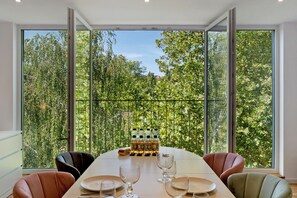 A dining area with a table set for four, large windows with a view of trees, and a bottle of water on the table. - Apartment 'Nagoldblick Liebeneckstraße' with Balcony and Wi-Fi (Pforzheim)