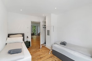 A modern bedroom with a bed, a bench, a wardrobe, and a door leading to a hallway.