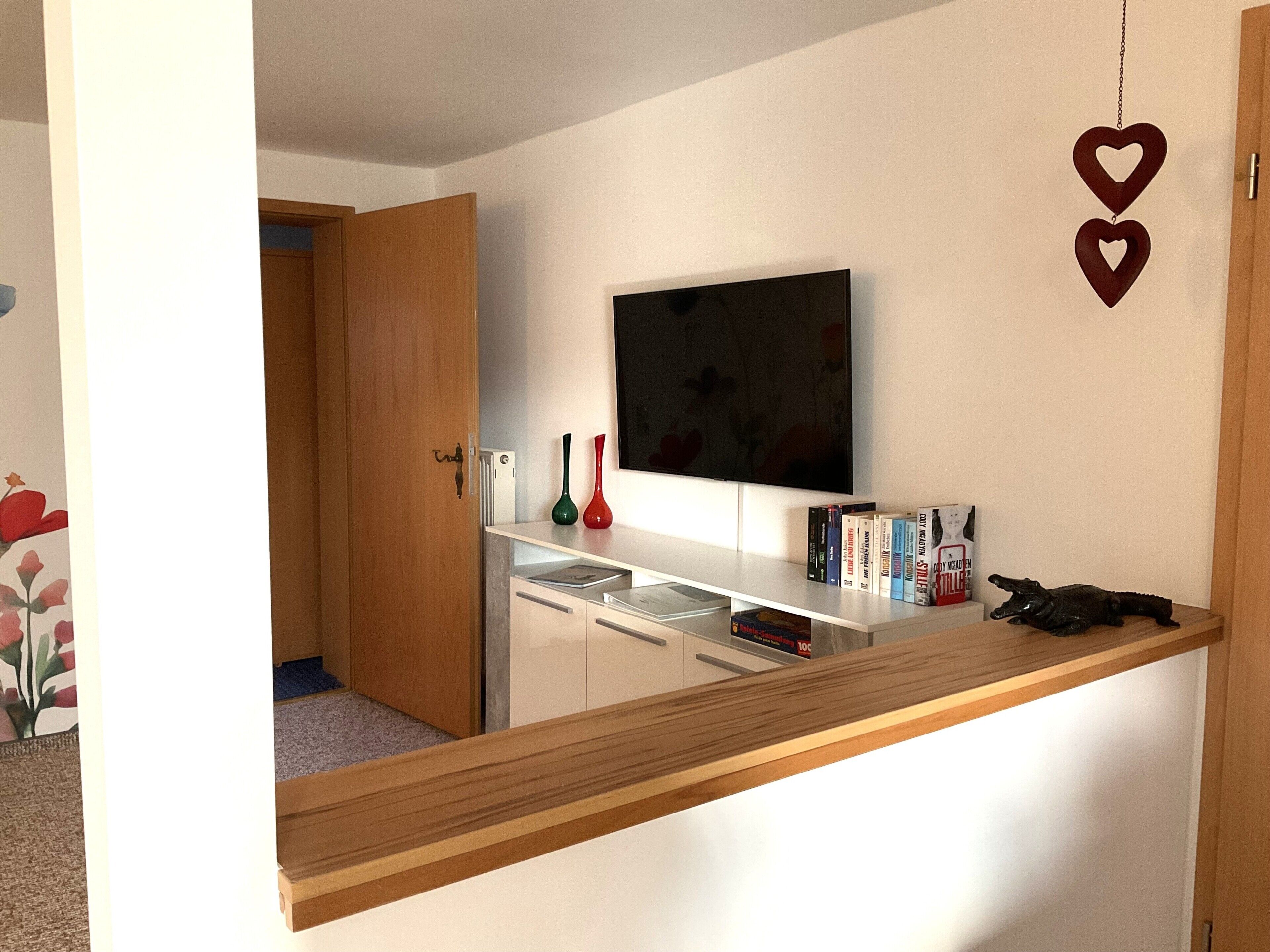 Una habitación con un escritorio de madera, un televisor de pantalla plana, una estantería y una puerta.