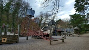 Un parque infantil con un puente de cuerdas, estructuras de madera y una torre de agua.