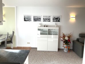 Un salon moderne comprenant un coin repas, un meuble blanc aux portes vitrées et trois photographies en noir et blanc accrochées au mur.