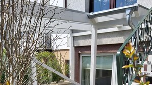 Un edificio moderno con un espacio exterior cubierto, una escalera y un jardín con flores rojas.