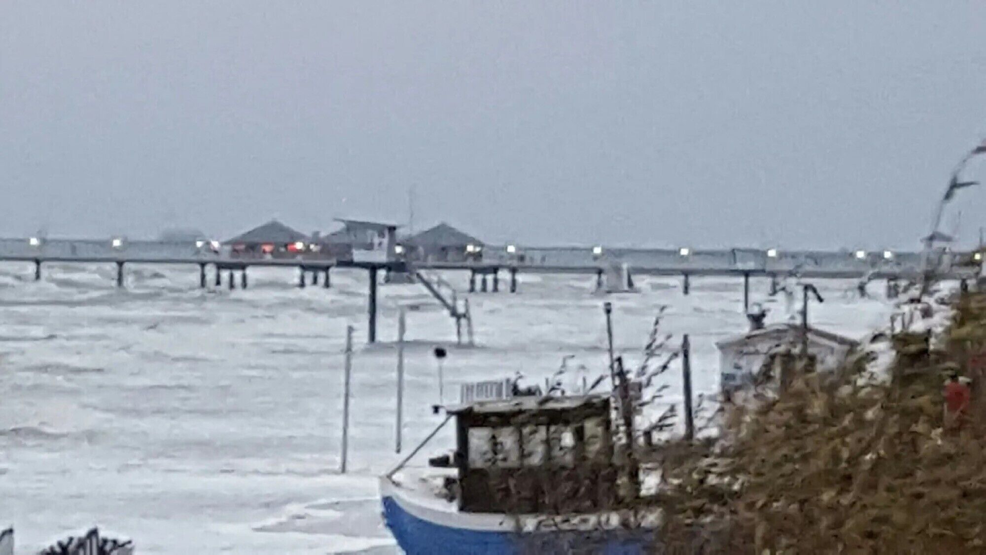 A pier extending into a stormy sea with a boat docked at the end.