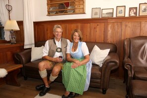 A couple seated on a brown leather sofa in a room with wooden paneling and a wooden cabinet above.