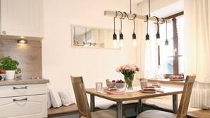 A dining area with a wooden table, four chairs, a vase of flowers, and a mirror above the table.