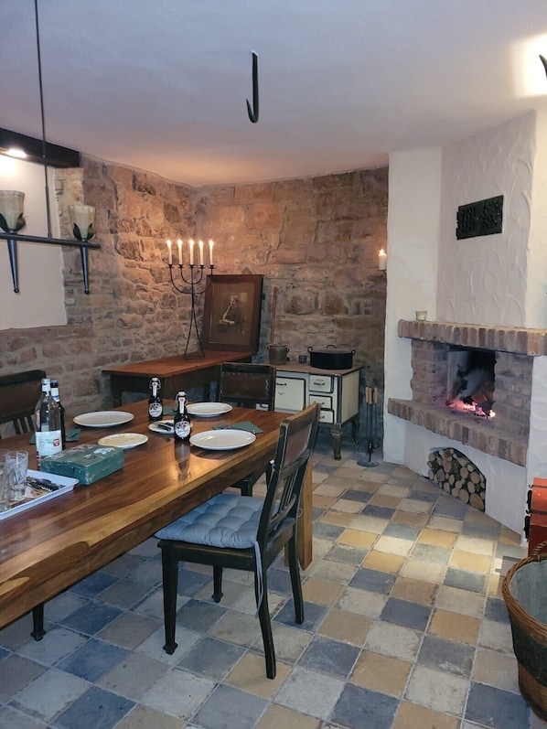 A dining area with a wooden table, chairs, a candelabra, and a stone wall.