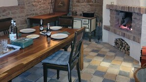 Uma sala de jantar com uma mesa de madeira, cadeiras, um candelabro e uma parede de pedra.