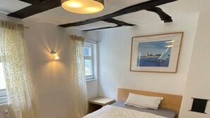 Een kamer met een bed, een raam met gordijnen, een wandlamp en een schilderij.