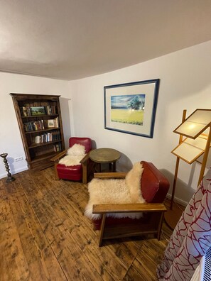 Un salon avec un plancher en bois, un canapé en cuir rouge, une petite table ronde, une bibliothèque et un tableau encadré au mur.