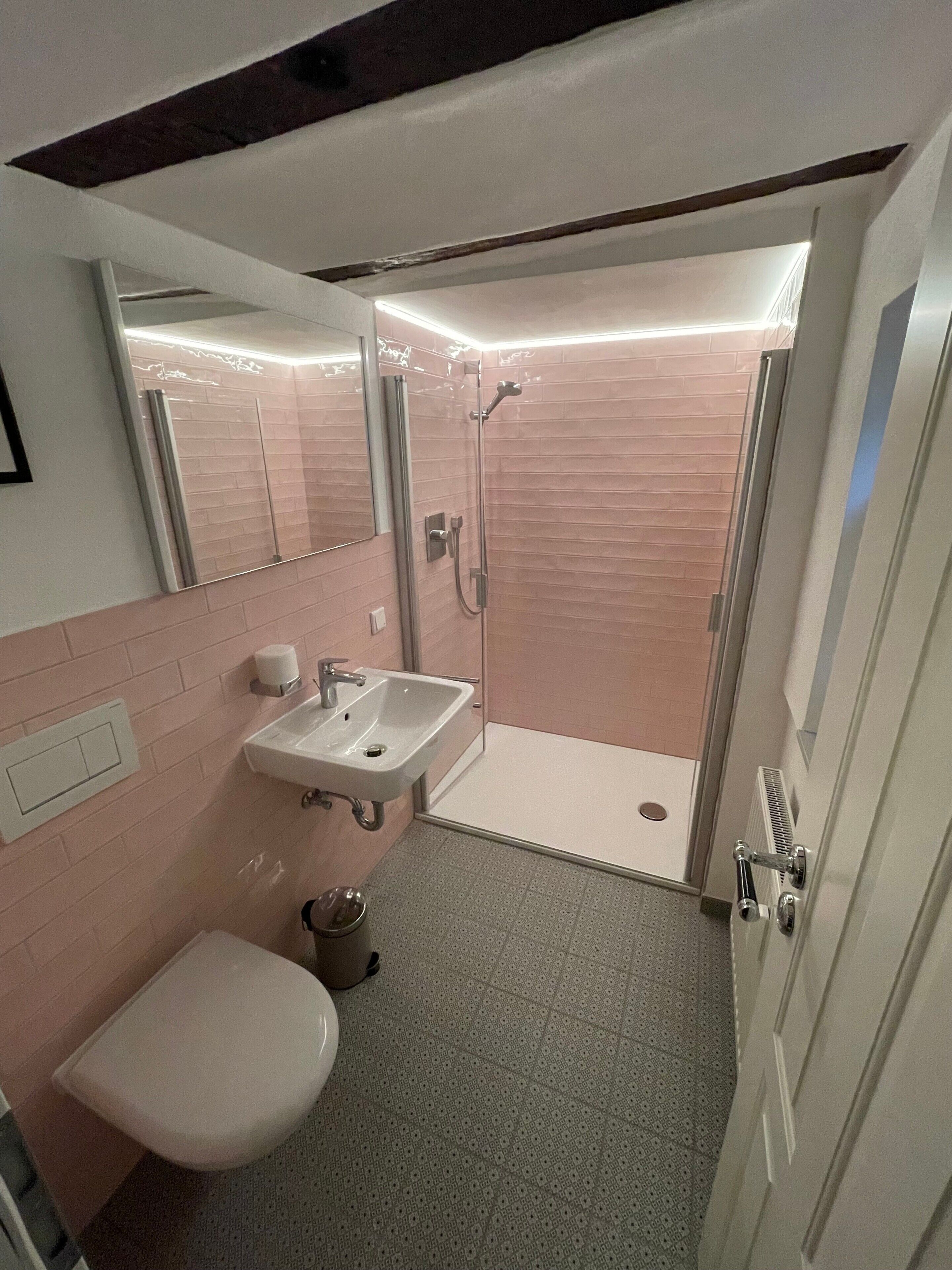 A bathroom with a shower, sink, toilet, and a mirror.