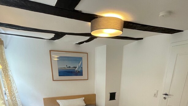 Een slaapkamer met een bed, nachtkastje, schilderij en een deur.
