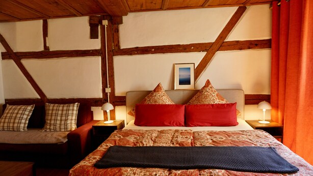 Une pièce avec un lit, un canapé, des poutres en bois et un tableau au mur.