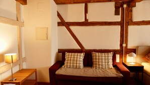 Une pièce chaleureuse avec un plancher en bois, un canapé rouge agrémenté de coussins à carreaux, une petite table en bois et une lampe posée sur une table d’appoint.