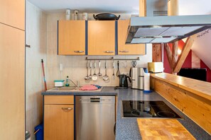 A compact kitchen with wooden cabinets, a dishwasher, a stove, and various utensils hanging above the counter. - Apartment 'Erlenblick' with Private Terrace, Shared Garden and Wi-Fi (Feldberger Seenlandschaft)