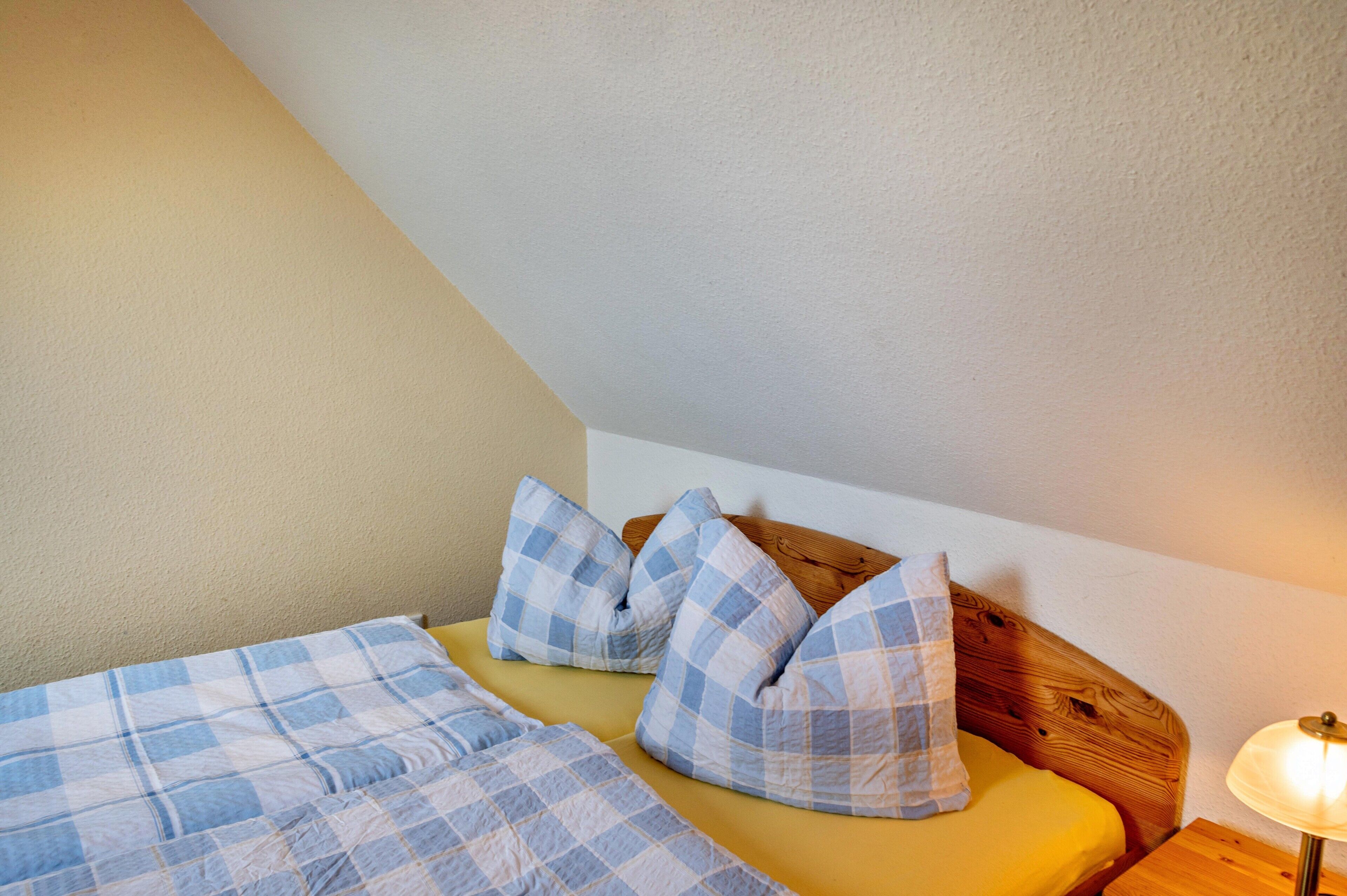 Een slaapkamer met een bed, geruit beddengoed, een houten hoofdbord en een bedlampje.