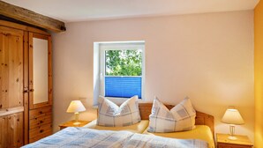 Une chambre à coucher comprenant un lit, deux tables de chevet, une fenêtre avec des stores et une armoire en bois.