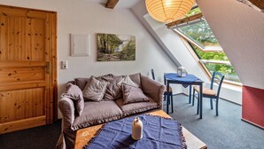 Una habitación acogedora con una puerta de madera, un sofá marrón, una mesa con un jarrón y vistas a través de un tragaluz.