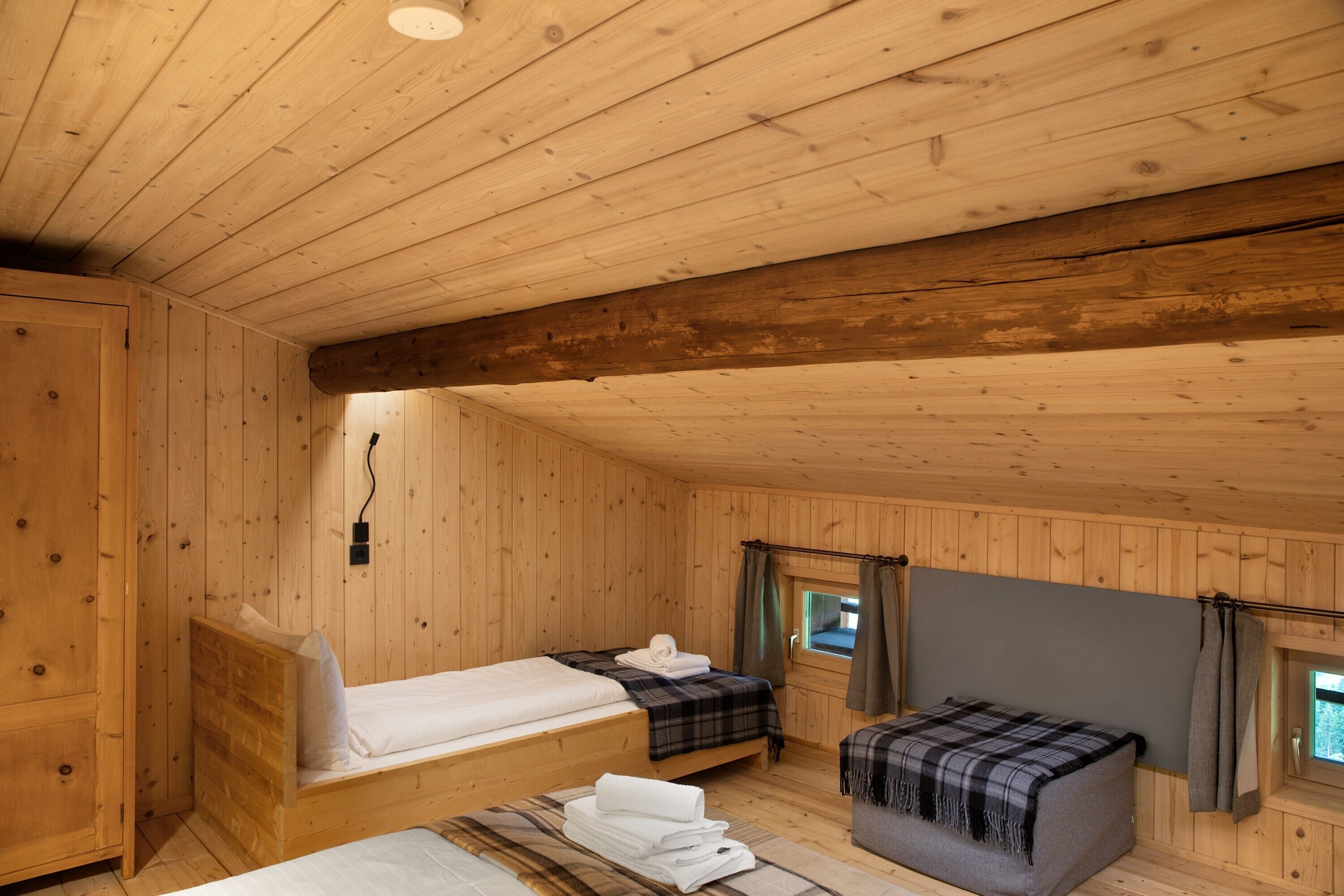 Uma cabana de madeira com duas camas, um sofá pequeno e uma janela com cortinas.