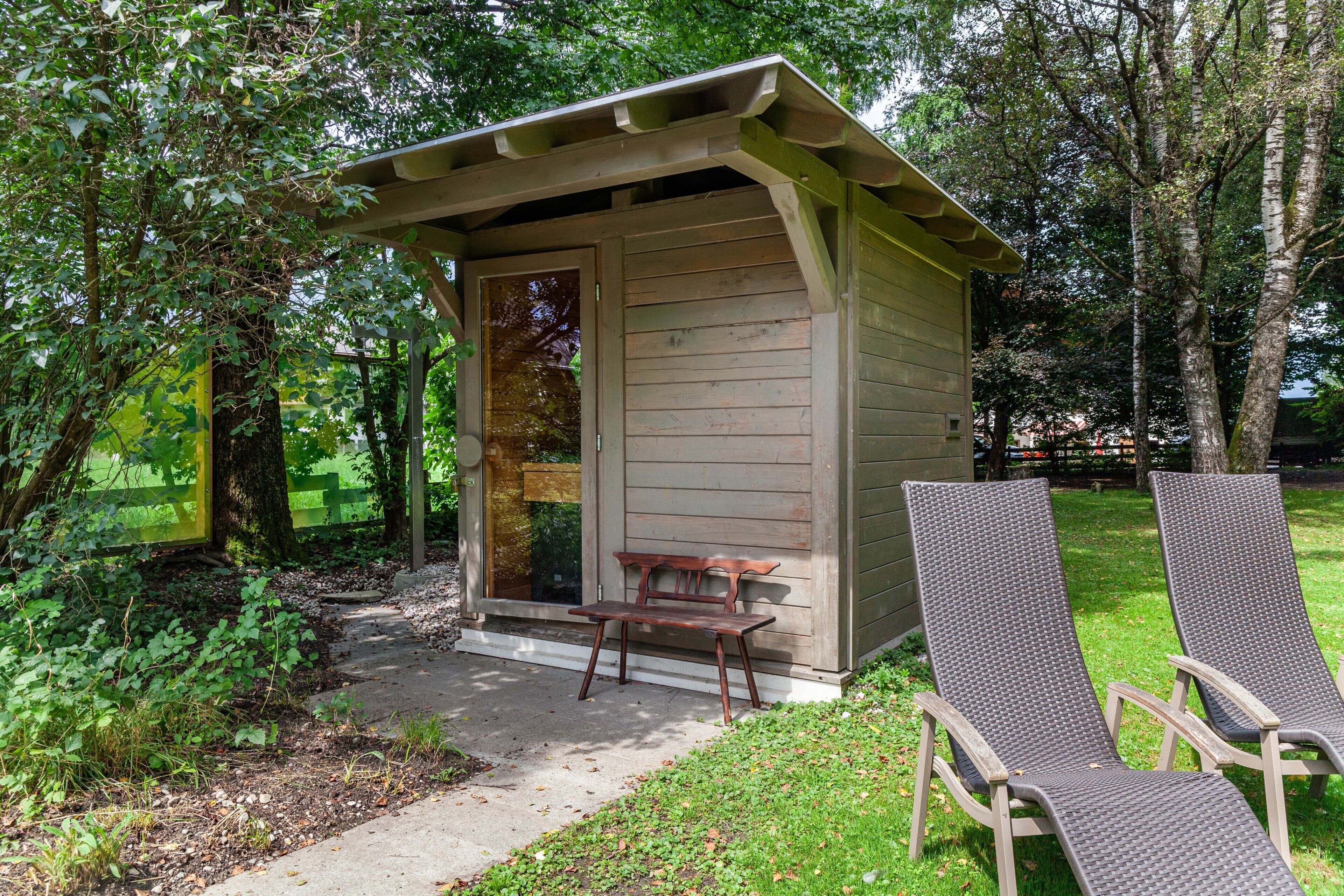 A wooden structure with a bench and two lounge chairs outside.