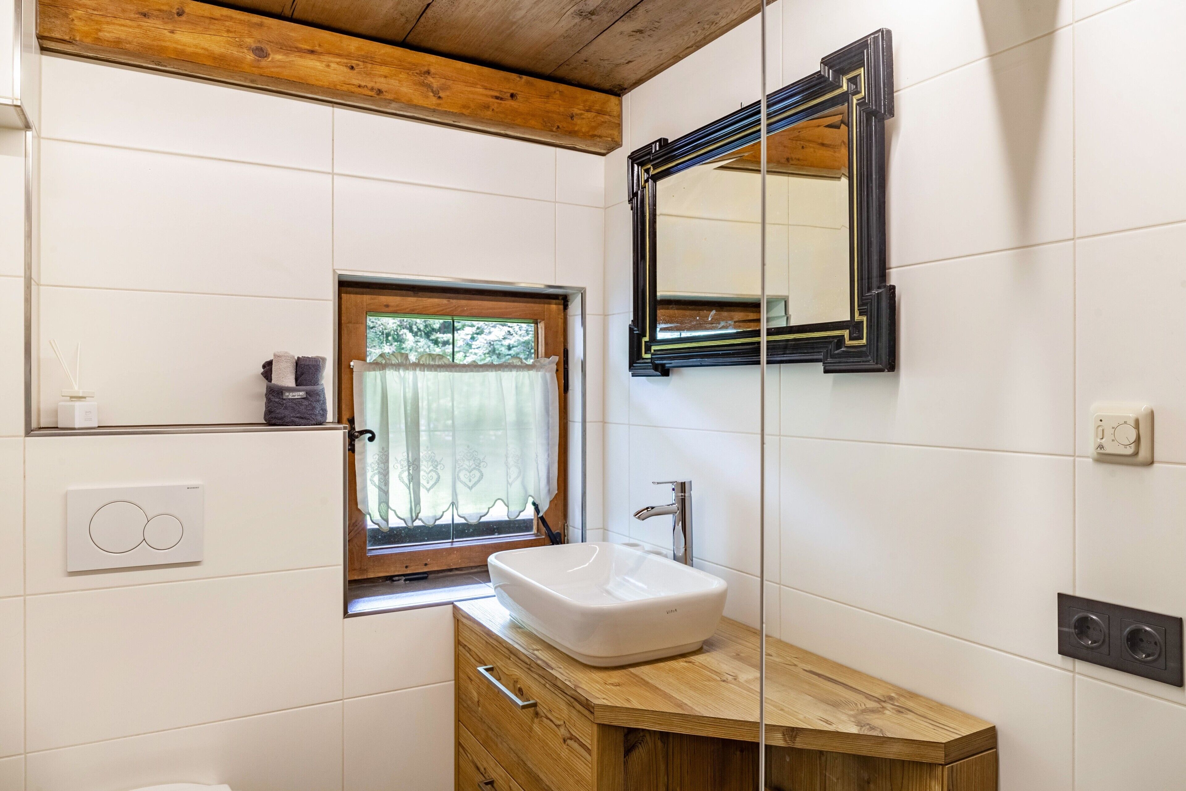 A bathroom with a wooden vanity, a white sink, a mirror, a window with a curtain, and a towel rack.