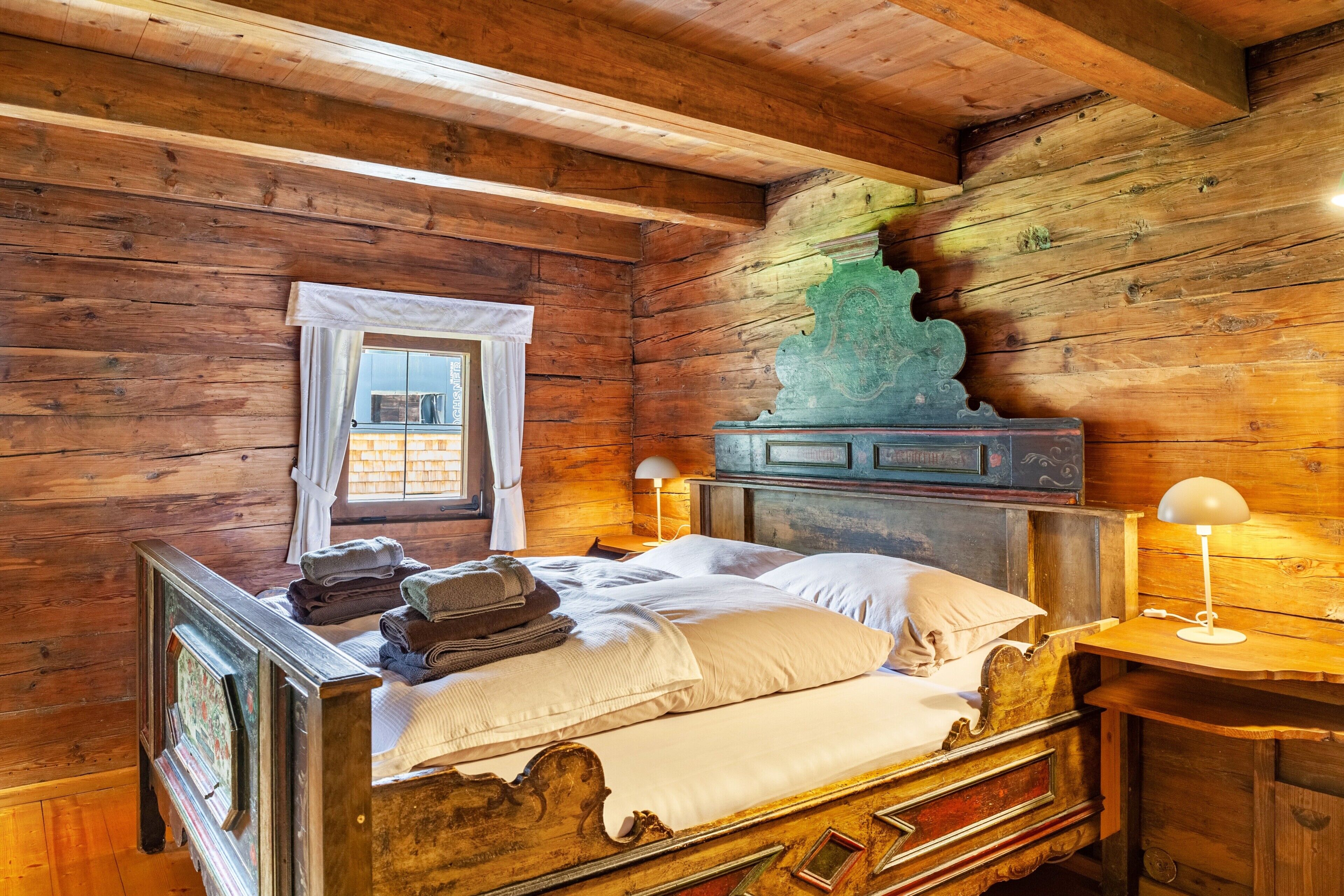 Ein holzgetäfelter Raum im Chalet-Stil mit Bett, Fenster mit Vorhängen, Lampe und einer Dekoration an der Wand.
